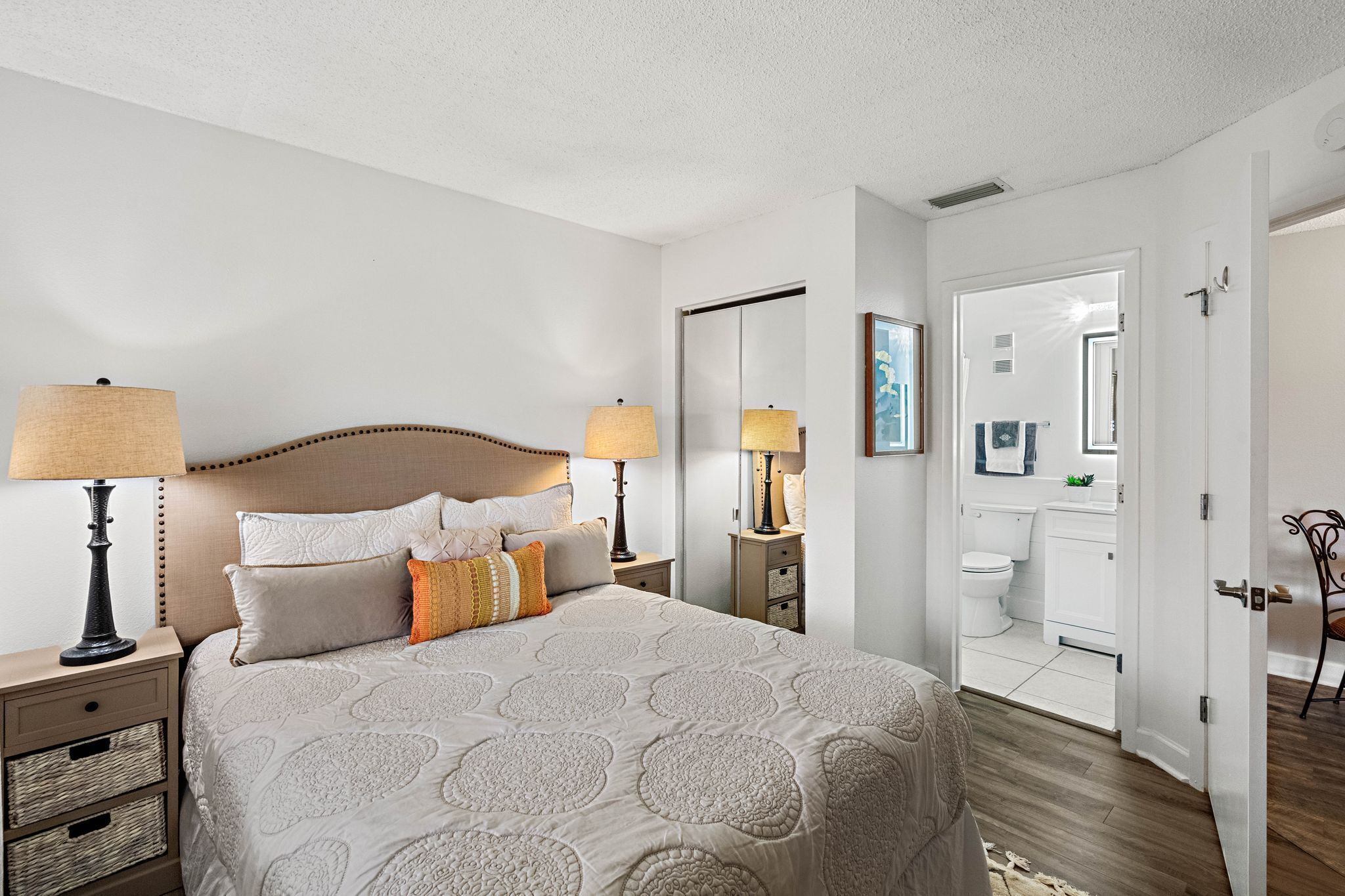 A hotel room with a bed, bedside lamps, a nightstand, a dresser, and a bathroom visible through an open door.