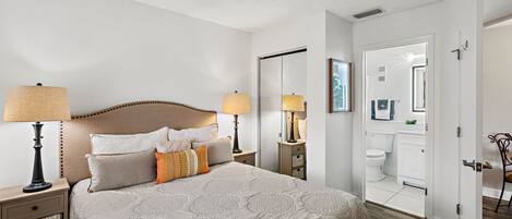 A hotel room with a bed, bedside lamps, a nightstand, a dresser, and a bathroom visible through an open door.