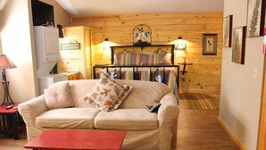 Una habitación acogedora con un sofá, una mesita, una cama con ropa de cama a rayas y una pared de madera.