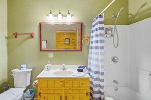 A bathroom with a wooden vanity, a white sink, a mirror, a shower curtain, and a toilet.