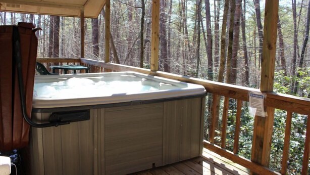 Un jacuzzi en una terraza de madera con vistas a un bosque.