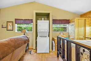 A compact kitchen with a built-in washer and dryer, wooden flooring, and windows with curtains.