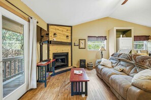 A cozy living room with a fireplace, a sofa, a table, and a window with curtains.