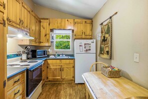 A compact kitchen with wooden cabinets, a microwave, a refrigerator, and a window with a view of greenery. - Cherokee Ridge 7 - Pet Friendly Cottage All About Location, Location (Sautee Nacoochee)