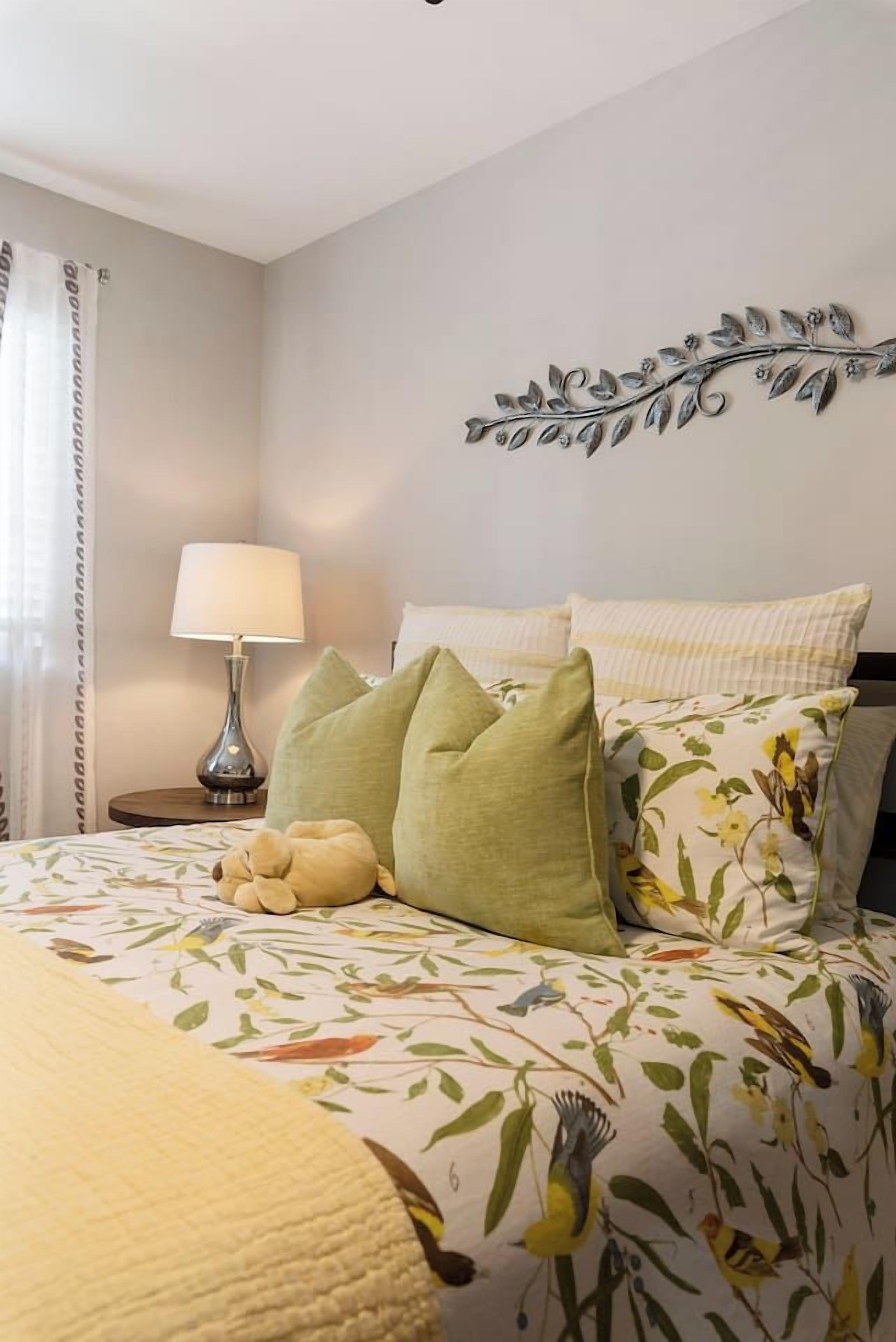 A neatly made bed with floral bedding, a decorative wall piece, and a bedside lamp.