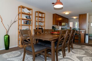 A dining area with a wooden table and chairs, surrounded by bookshelves, in a well-lit room with wooden cabinets and a patterned rug.