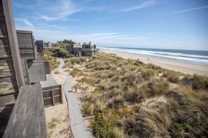 Una propiedad costera con una terraza de madera, un sendero arenoso y vista a la playa y al océano.