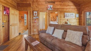 A wooden cabin interior with a couch, a bench, a sign reading 'Couple's Retreat,' and a door leading to another room. - Couples Retreat - Romantic and Relaxing Cabin Retreat (Cleveland)