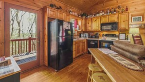 A wooden cabin with a kitchen, dining area, and a deck with a view of trees. - Couples Retreat - Romantic and Relaxing Cabin Retreat (Cleveland)