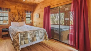 A wooden cabin bedroom with a bed, a nightstand, a ceiling fan, and a sliding glass door to a balcony. - Couples Retreat - Romantic and Relaxing Cabin Retreat (Cleveland)