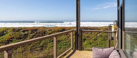 Un balcone con vista sull'oceano, un'area salotto con cuscini e una ringhiera.