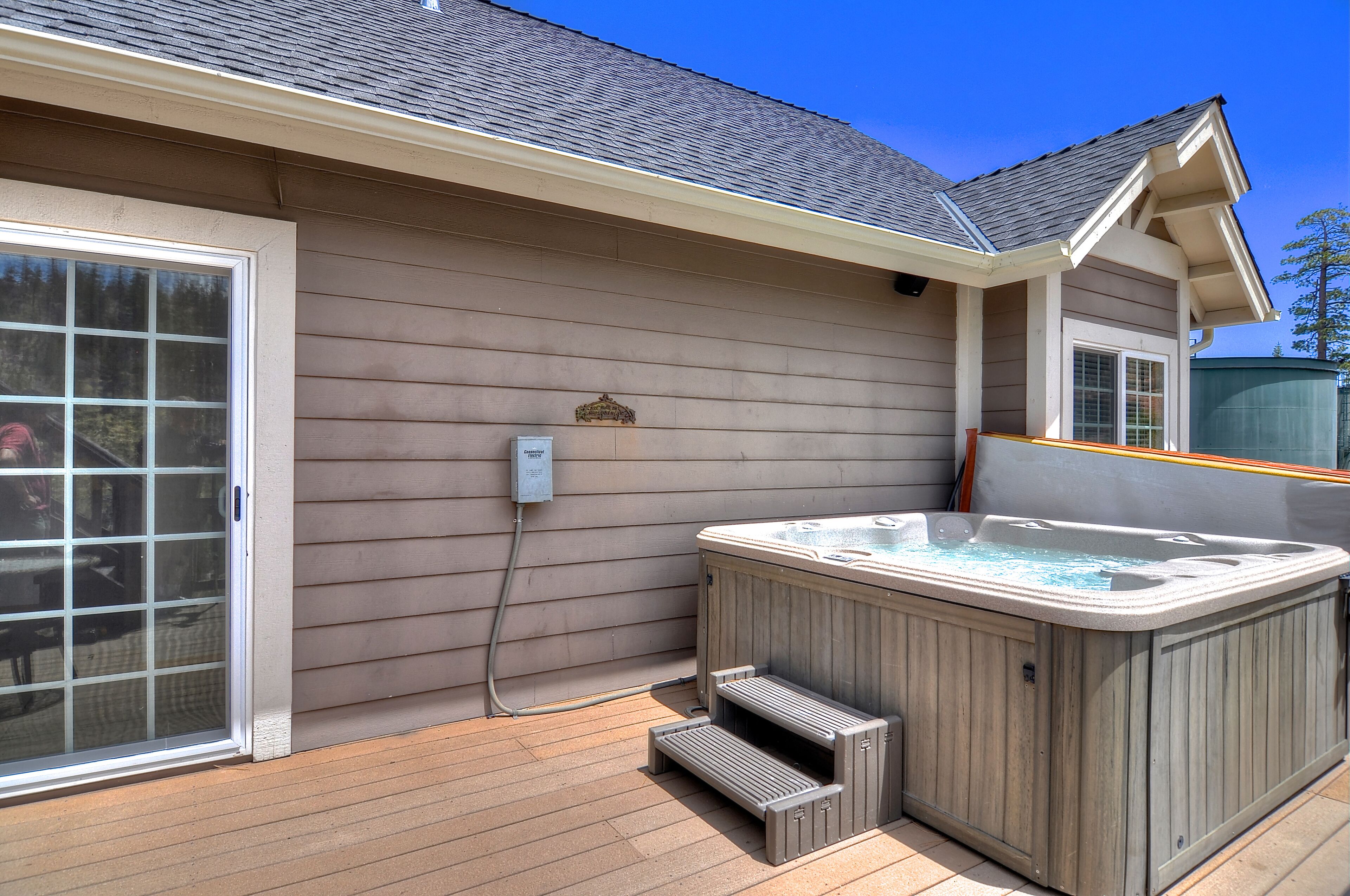 Jacuzzi exterior d'una casa amb terrassa de fusta, porta corredissa de vidre i presa elèctrica a la paret.