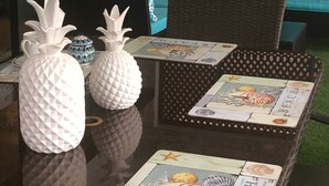 Pöytä, jossa on koriste-esineitä ja lautapeli, rottinkituoli sekä turkoosi sohva, jossa on kuvioidut koristetyynyt.