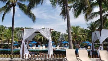 Un entorno de resort con piscina, sillas de descanso y una estructura tipo pérgola.