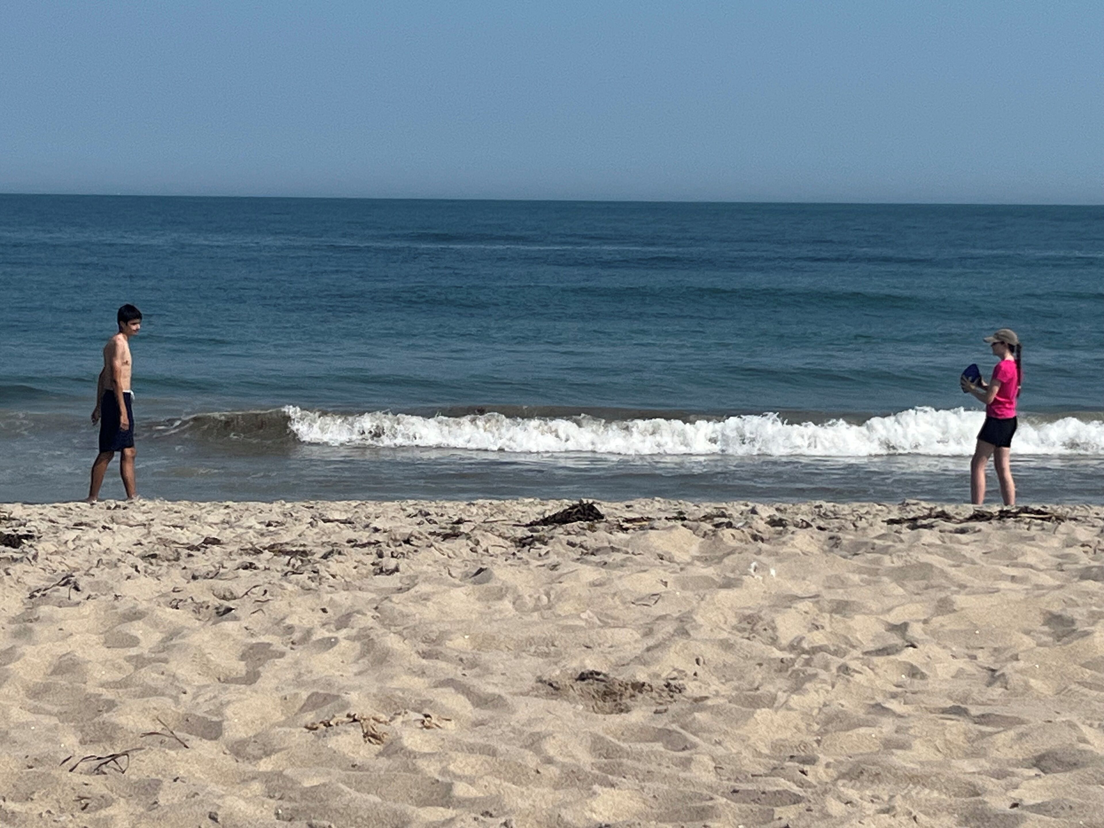 A beach with two people standing on the sand, facing the ocean.