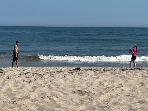 Une plage où deux personnes se tiennent sur le sable, face à l’océan.
