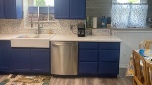 Une cuisine avec des meubles bleus, un lave-vaisselle en acier inoxydable, une machine à café et un panneau décoratif sur le thème de la plage.
