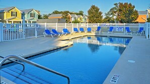Una piscina con sillas azules y una valla blanca, rodeada de casas.
