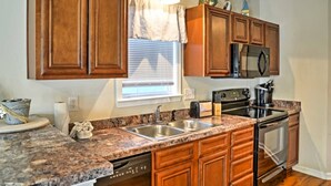 Una cocina con armarios de madera, encimeras de granito, microondas, estufa y lavavajillas.
