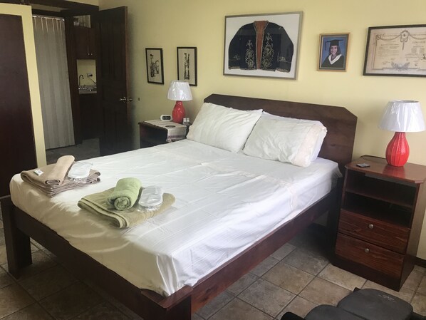 A neatly made bed with white linens, a red lamp, and a bedside table with a phone and a red vase.