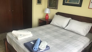 A neatly made bed with white and blue towels, a red lamp, and a nightstand with a framed picture. - Deluxe Two-Bedroom Apartment in Escalante, San Jose center. (San José)