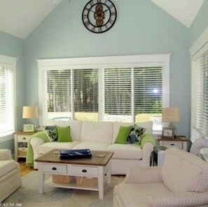 Relax in this spacious living room with a sofa, table, and clock, surrounded by natural light and a high ceiling.