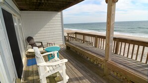 A wooden deck with a view of the beach, a covered area with a table and chairs, and a wooden railing.
