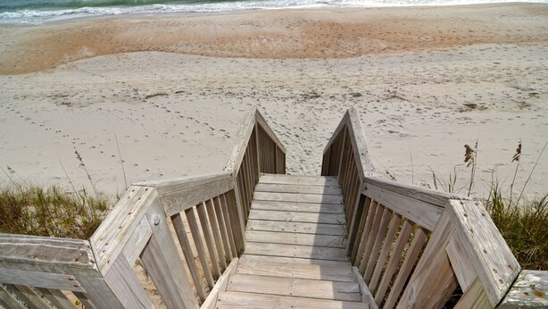 A wooden staircase leading to a sandy beach with ocean waves in the background.