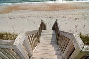 A wooden staircase leading to a sandy beach with ocean waves in the background. - Queen's Grant Oceanfront Condo, Topsail Beach, 1st Floor, Pool, Boat access. (Topsail Beach)