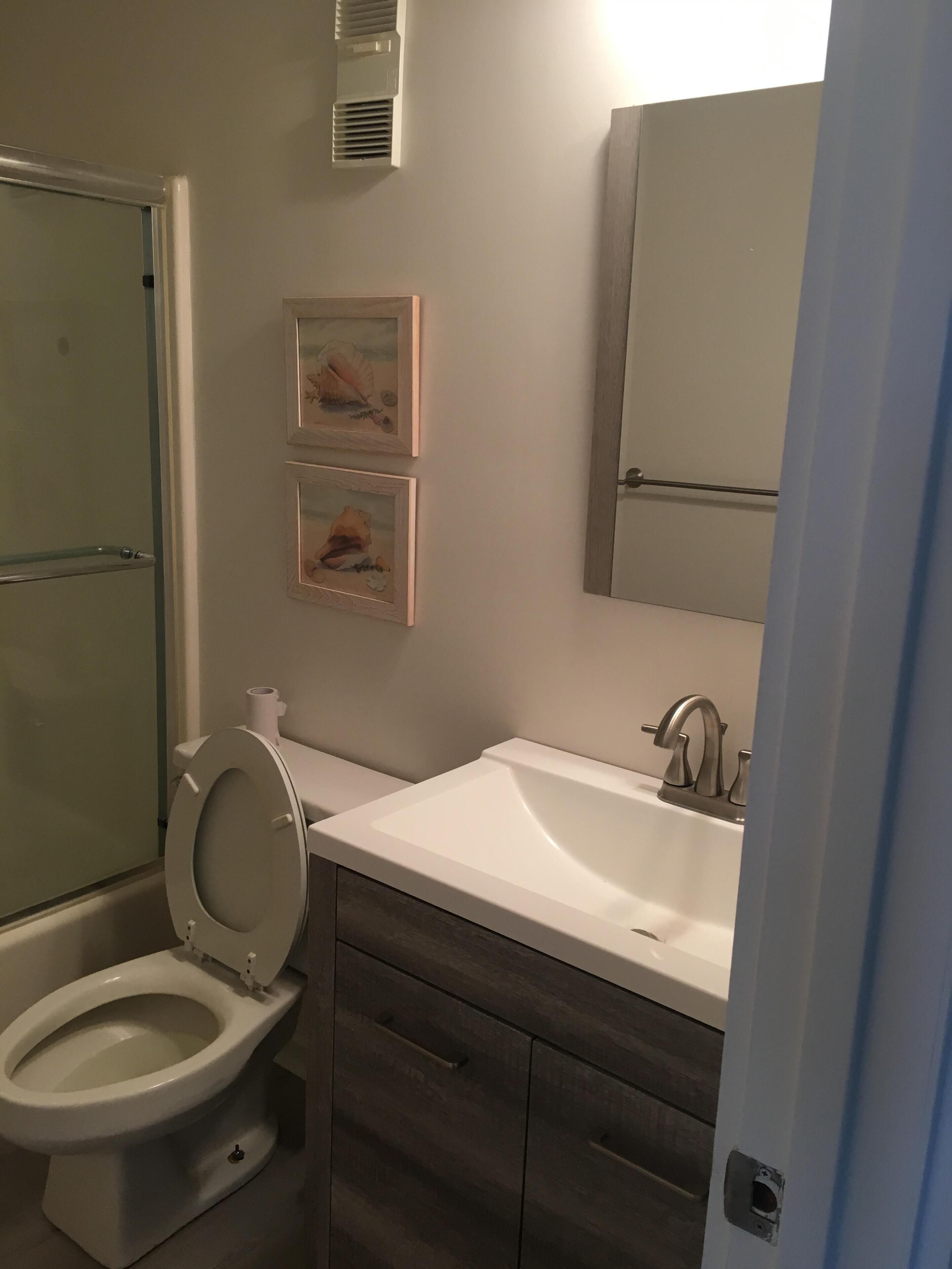 A bathroom with a toilet, sink, and mirror. There are two framed pictures on the wall.
