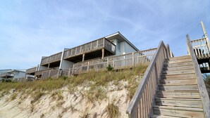 A beachfront property with a wooden deck leading to a building with multiple balconies.
