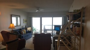 A living room with a sofa, chairs, a lamp, a bookshelf, and a television.
