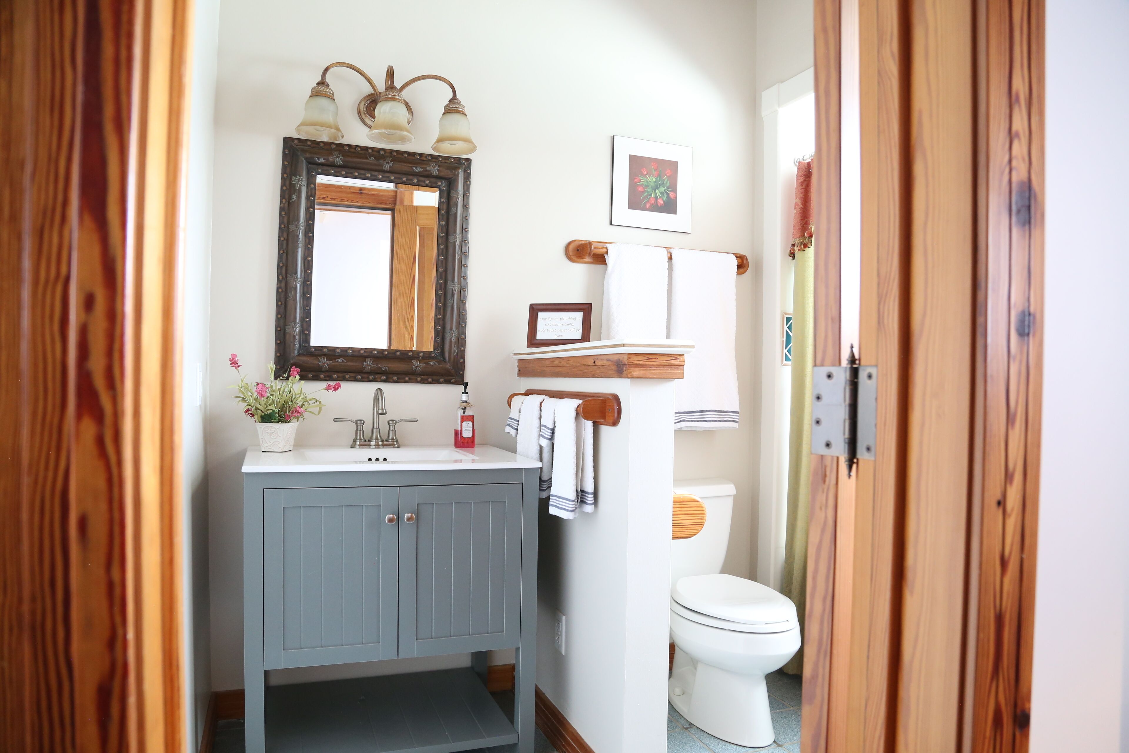 Un baño con tocador de madera, espejo, lavamanos e inodoro.