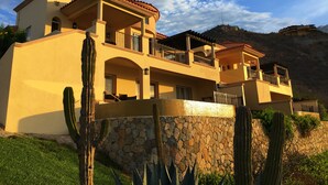 A multi-story building with balconies, a stone wall, and cacti.