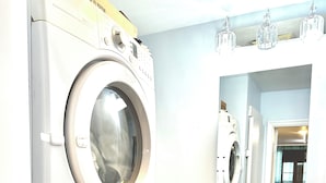 Une petite buanderie comprenant une machine à laver et un sèche-linge superposés, un petit évier avec un miroir au-dessus, et un meuble avec des tiroirs.