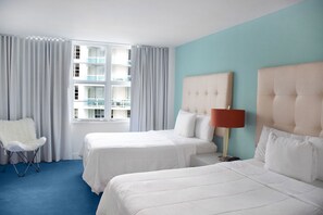 A hotel room with two beds, a chair, a lamp, and a view of a building through large windows.