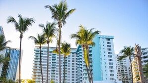 A high-rise hotel with multiple floors, palm trees in the foreground, and a white fence. - 1bd Bayfront Ste BayView w/ Balcony, Pool, nearby dining, beach access (Miami Beach)