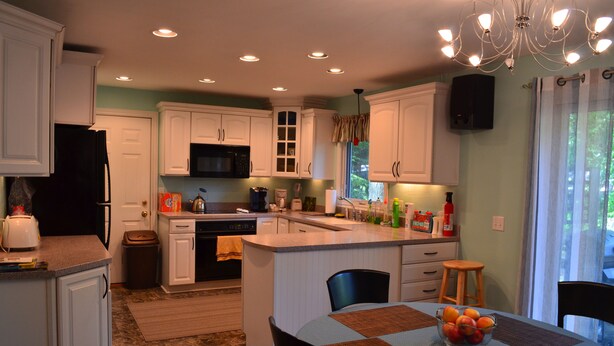 A kitchen with white cabinets, a central island, a dining table with a placemat, and a chandelier.