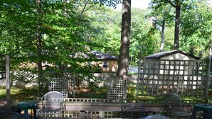 An outdoor patio area with metal tables and chairs, surrounded by a wooden fence and trees.