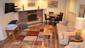 A living room with a fireplace, a sofa, a dining table with chairs, and a TV mounted on the wall.