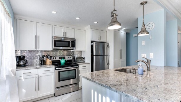 A modern kitchen with white cabinets, stainless steel appliances, a granite countertop, and pendant lighting.