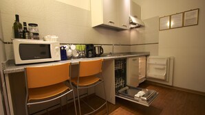 Een kleine keuken met een magnetron, twee barkrukken, een koffiezetapparaat en een vaatwasser.