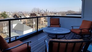 Ein Balkon mit Tisch und Stühlen, mit Blick auf eine Stadtlandschaft mit Gebäuden und einer Brücke.