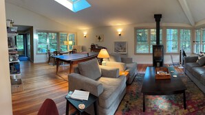 Ein geräumiges Wohnzimmer mit Kamin, großen Fenstern, einer Couch, einem Couchtisch und einem Essbereich mit Tisch und Stühlen.