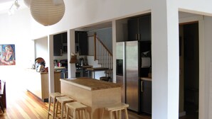Eine moderne Küche mit Holzstühlen, einer zentralen Kochinsel, Edelstahlgeräten und einer Treppe zu einer weiteren Ebene.