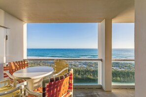 Un balcon avec une table et des chaises, donnant sur une plage et l’océan.