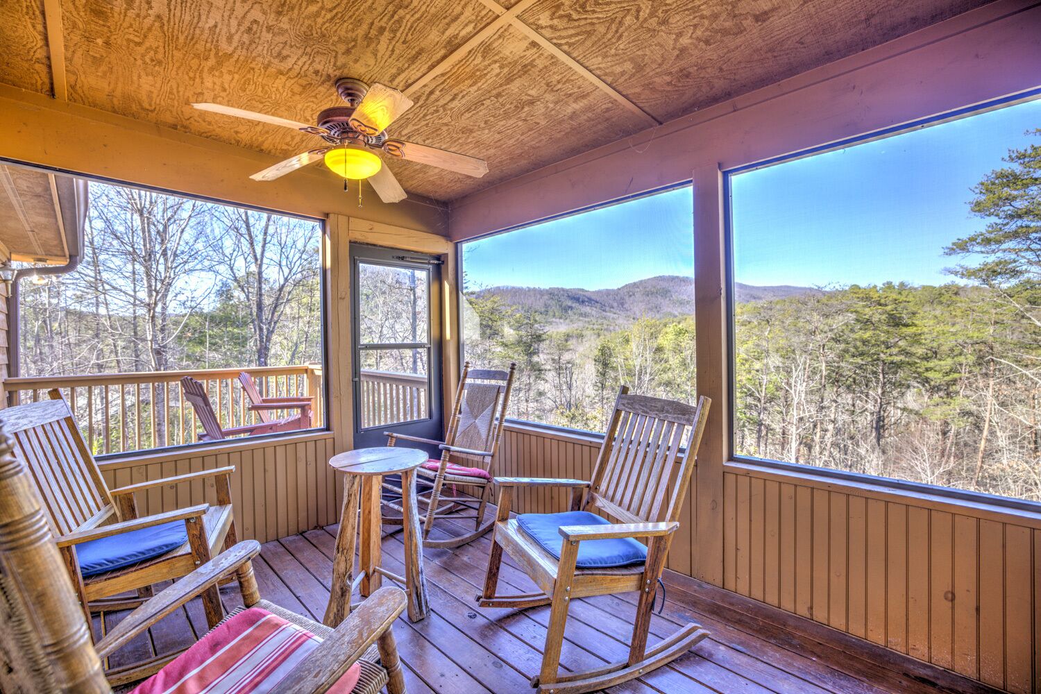 A wooden deck with rocking chairs and a table, overlooking a forested landscape.