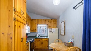 A compact kitchen with wooden cabinets, a refrigerator, a microwave, and a window.