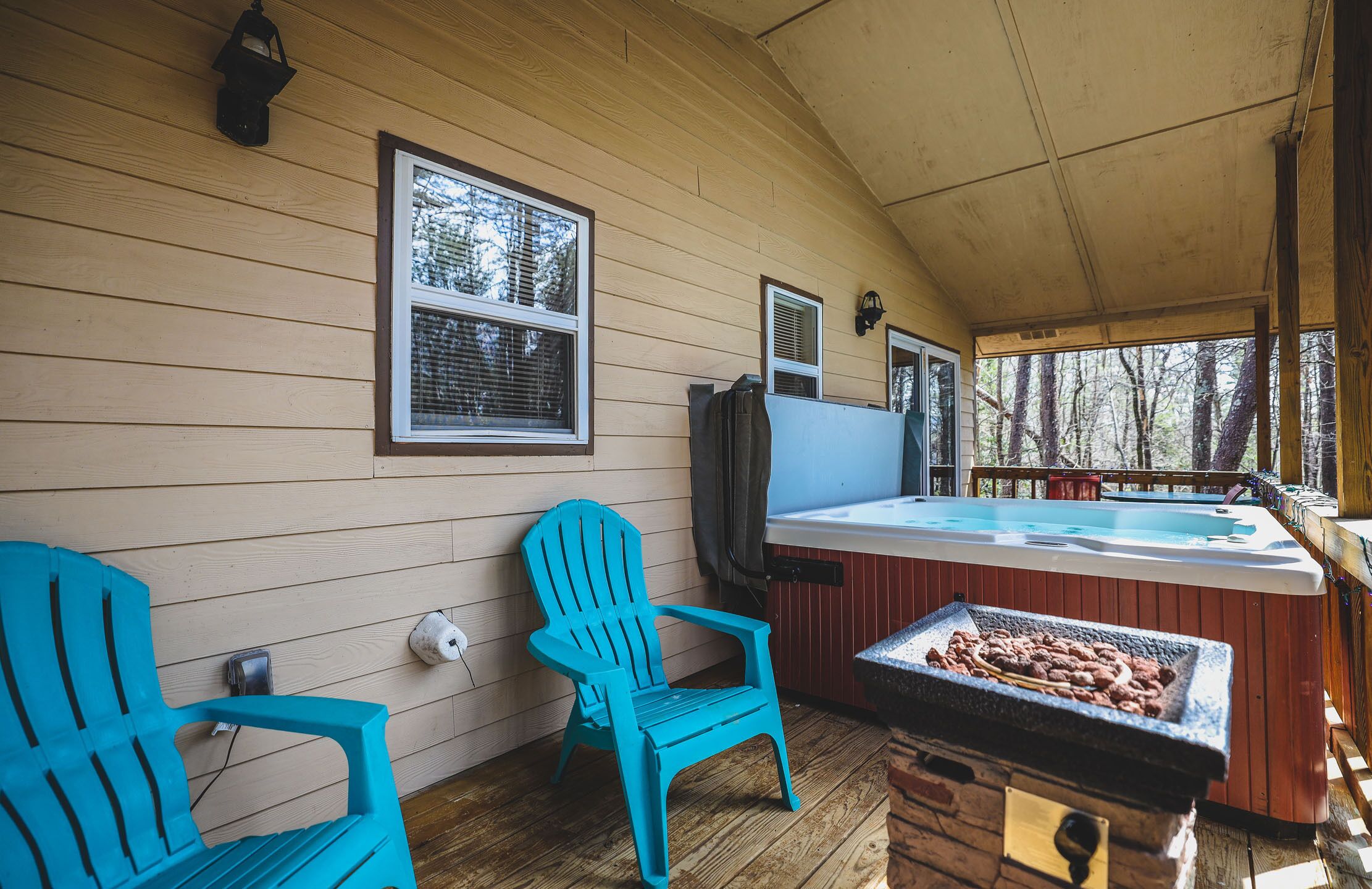 Una terraza de madera con un jacuzzi, dos sillas Adirondack y una parrilla.