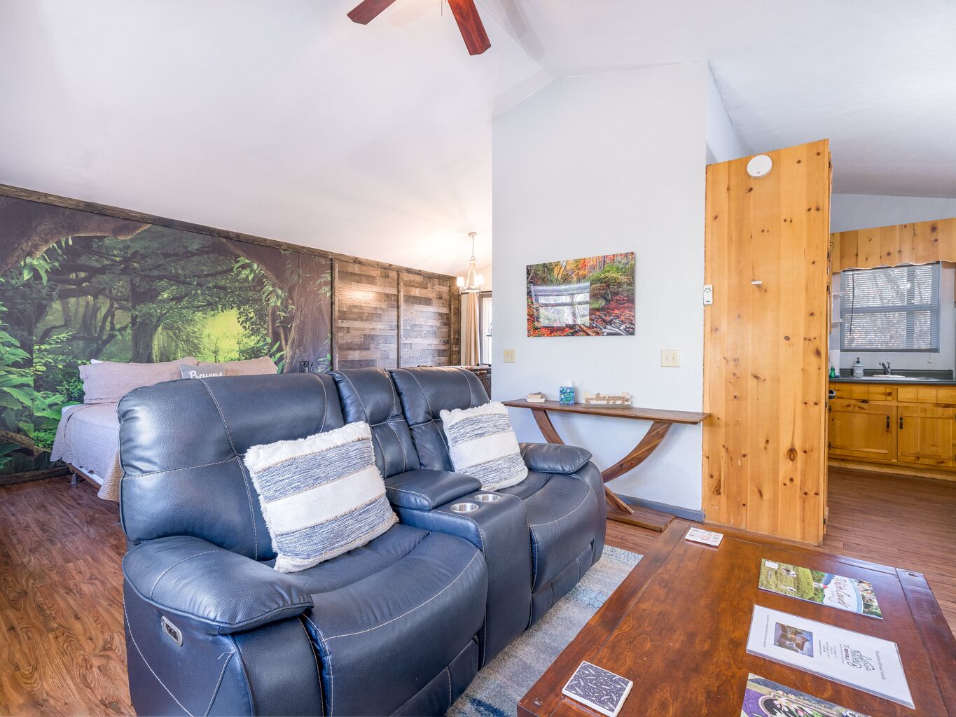 Una sala de estar moderna con un sofá de cuero, una mesa de centro de madera y una cocina visible a través de una puerta abierta.